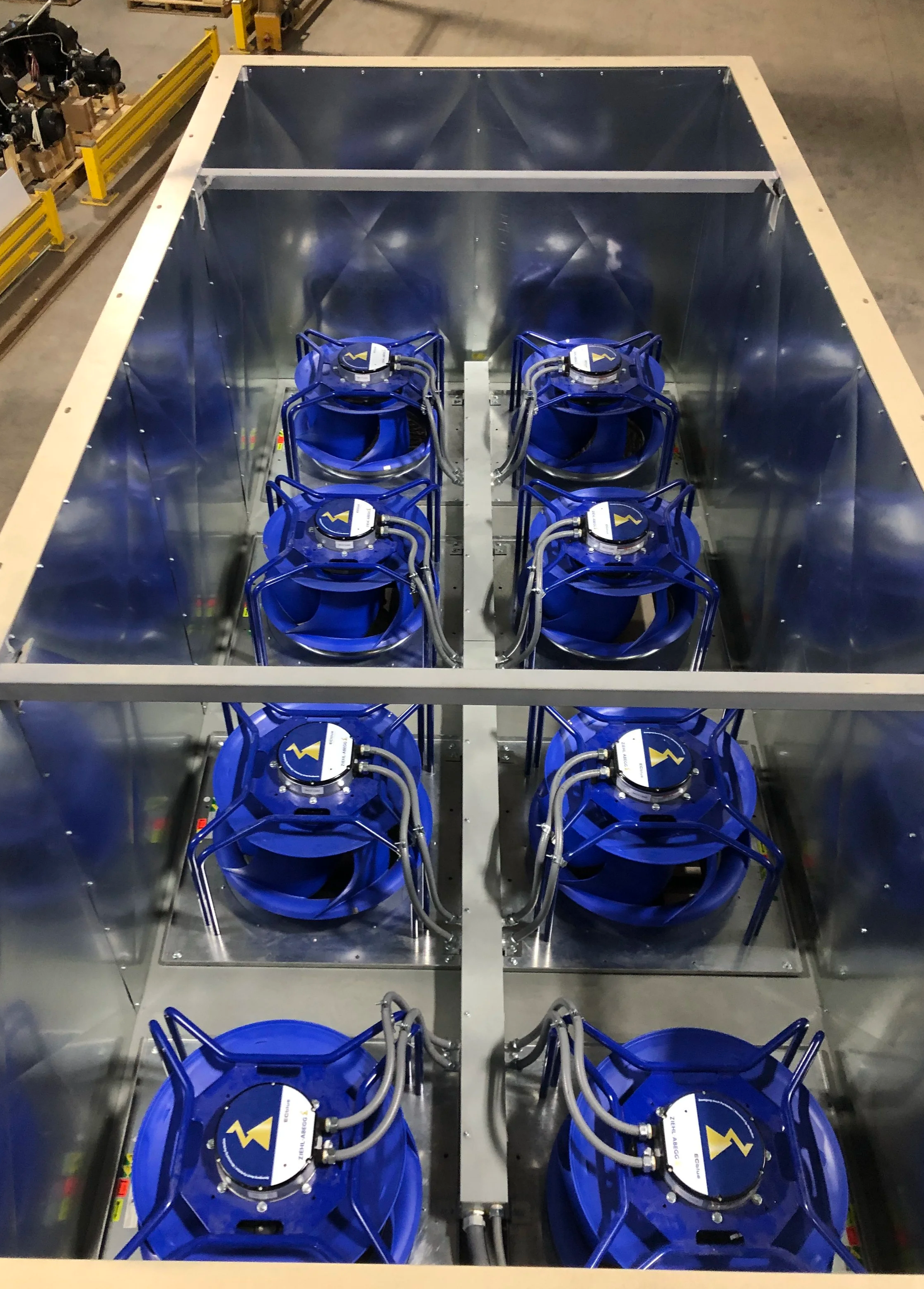 Eight (8) blue ECM fans inside an air-rotation unit, arranged in two rows of four, with cables connected to each fan.