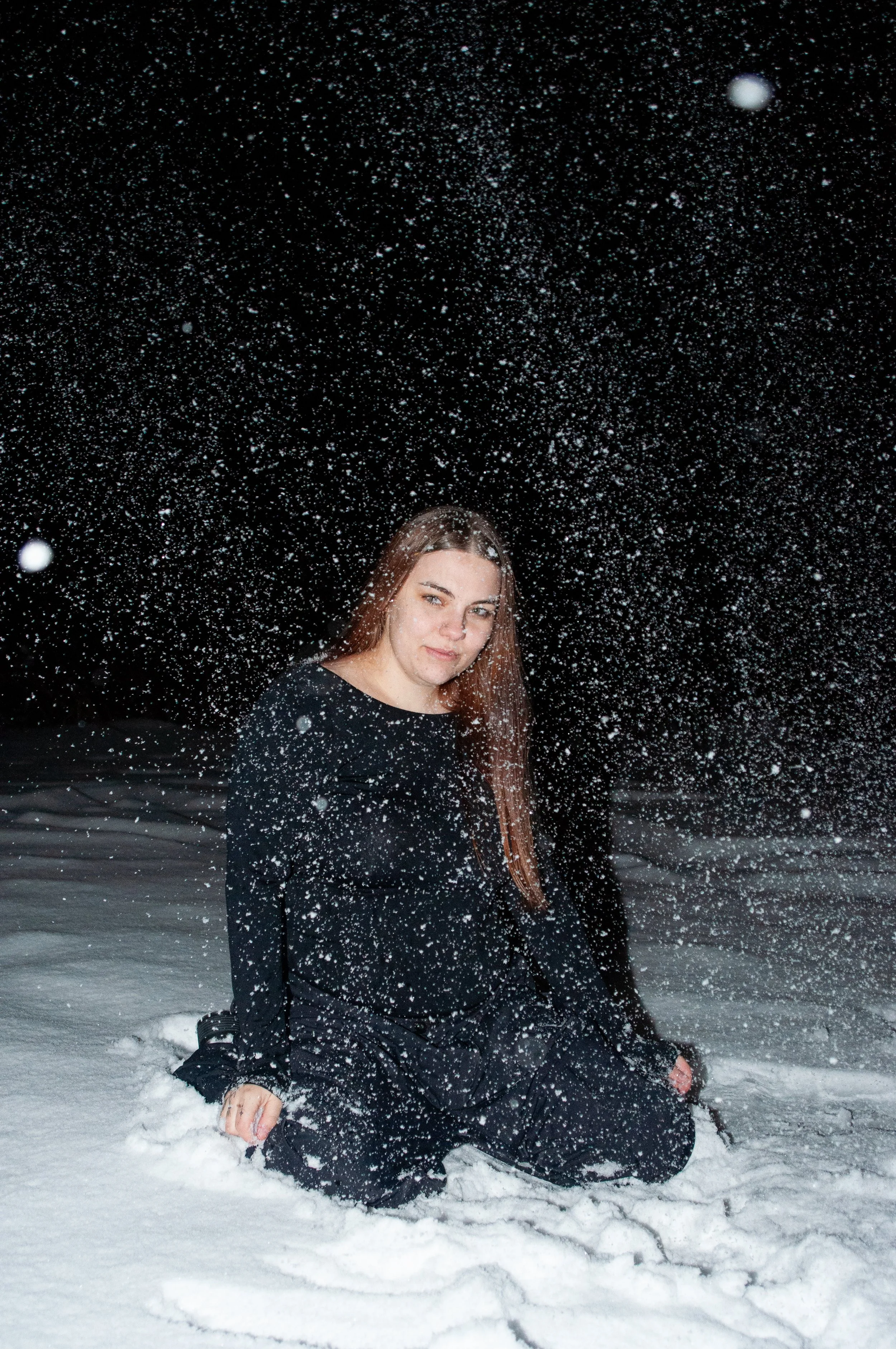 A woman kneeling in the snow during a snowstorm at night, with snow falling around her.