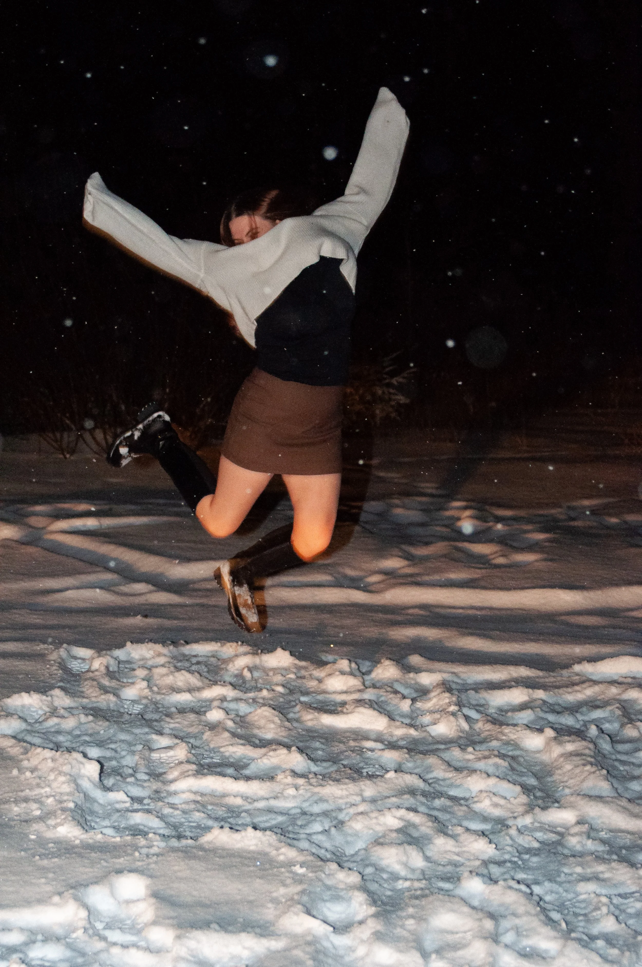Person jumping in the snow at night with snow falling around.