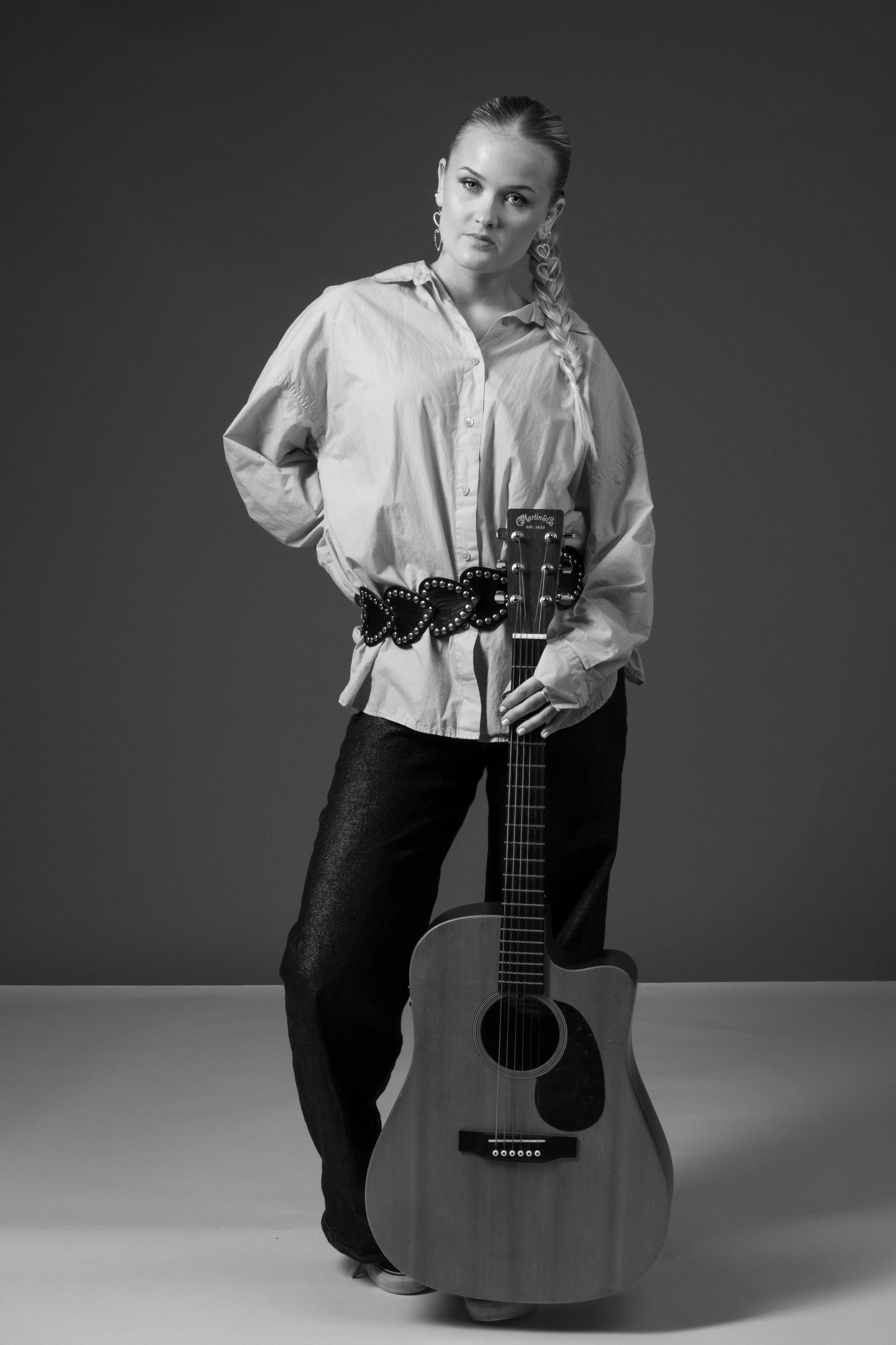 A woman with braided hair holding an acoustic guitar in a studio, black and white photo.