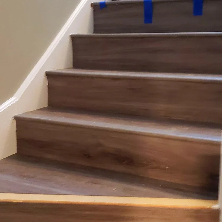 Newly installed hardwood stairs with blue painter's tape on the stair railing.