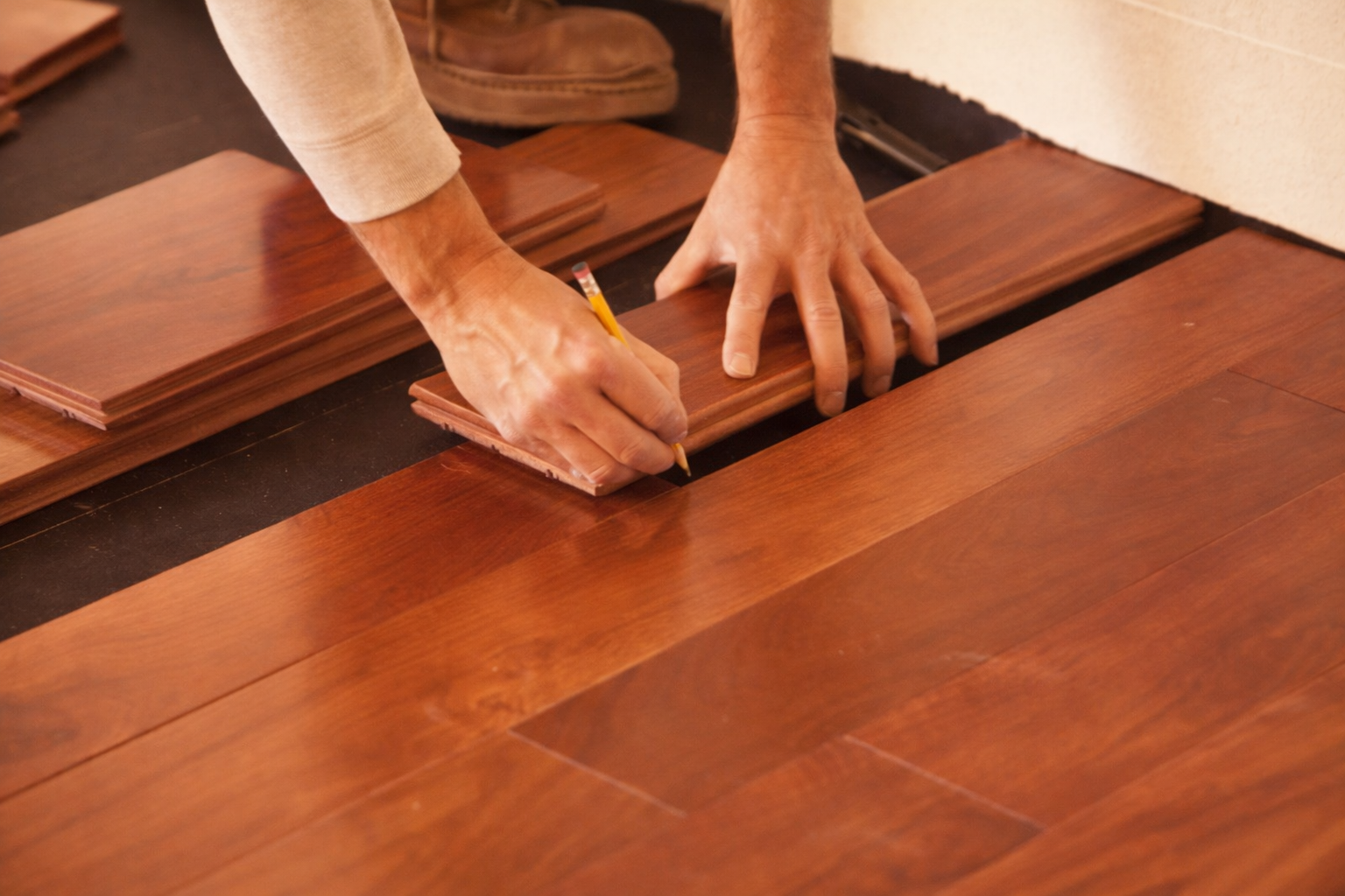 Person installing wooden flooring with a pencil and measuring tools.