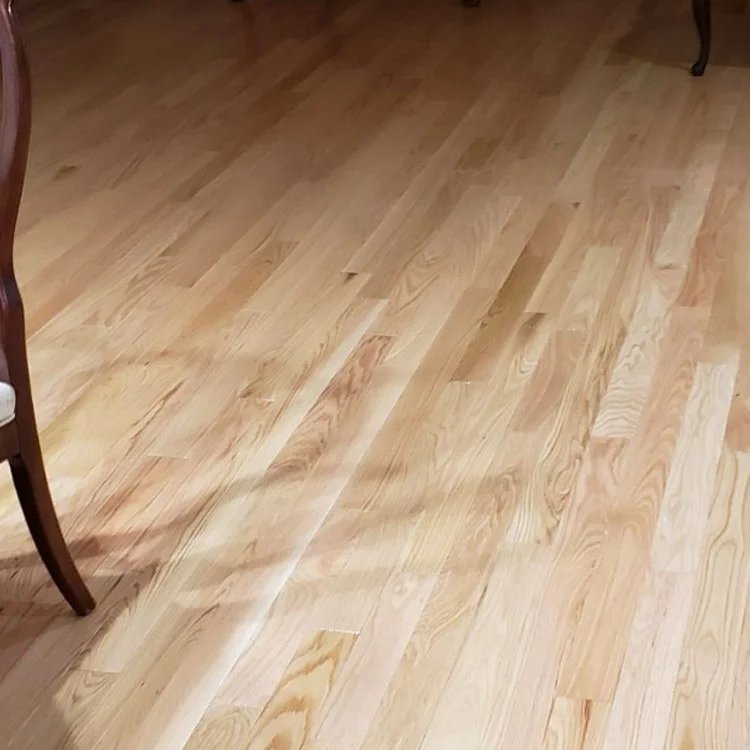 Wooden floor with light-colored planks and part of a chair in the corner.