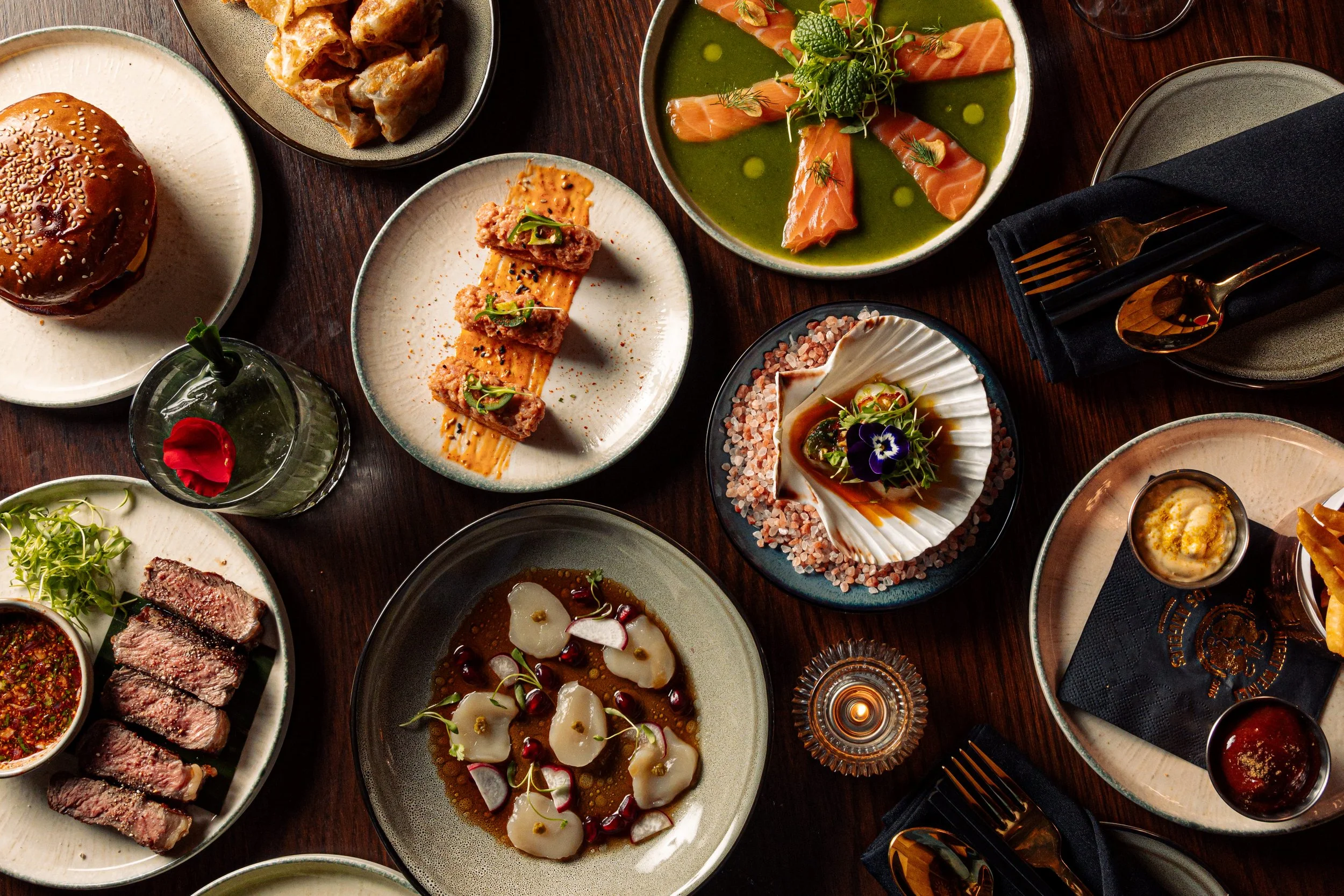 Full table of Pan Asian dishes on a dark wood table, viewed from above.