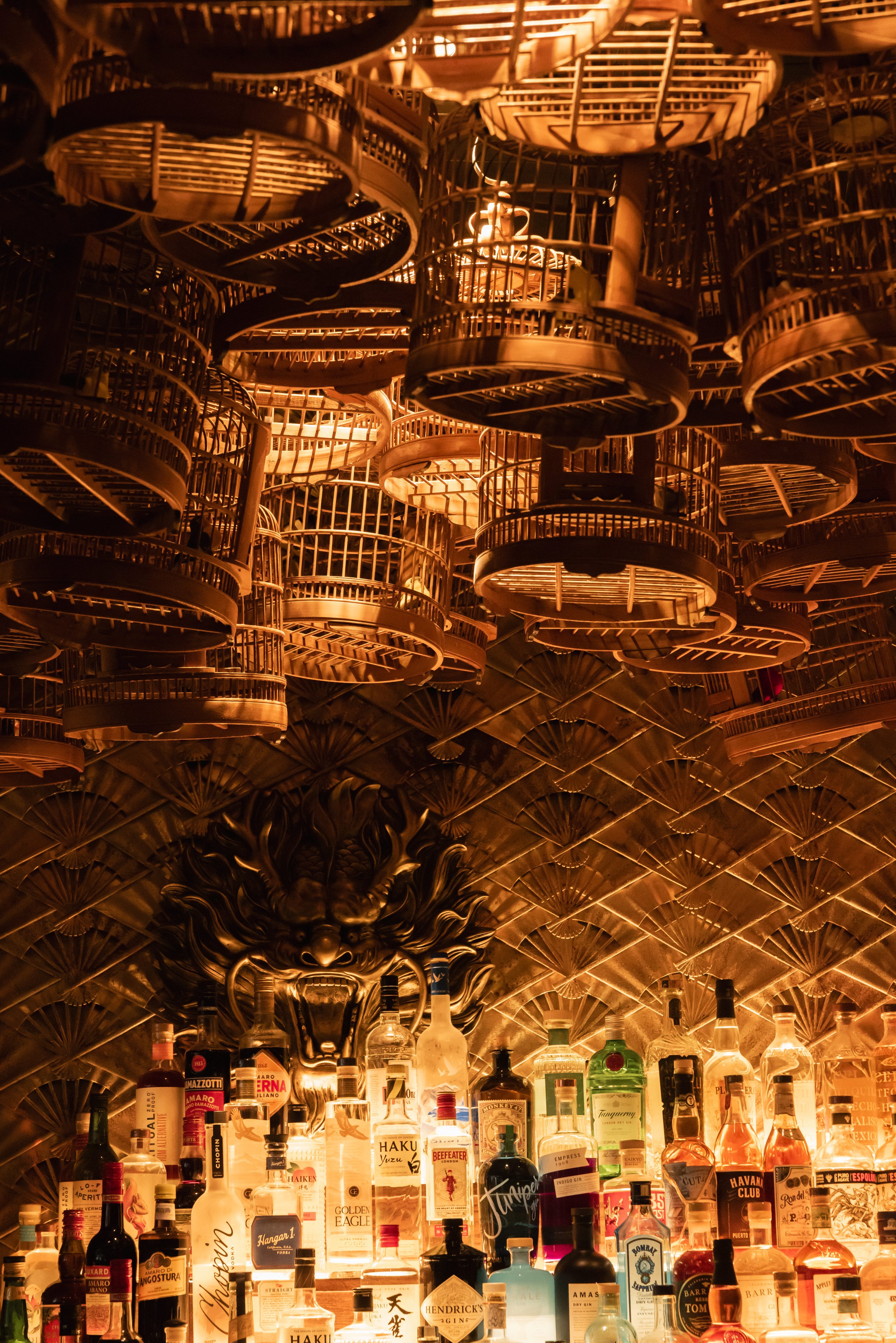 Decorative birdcages hang above a multi-tiered shelf of liquor bottles.
