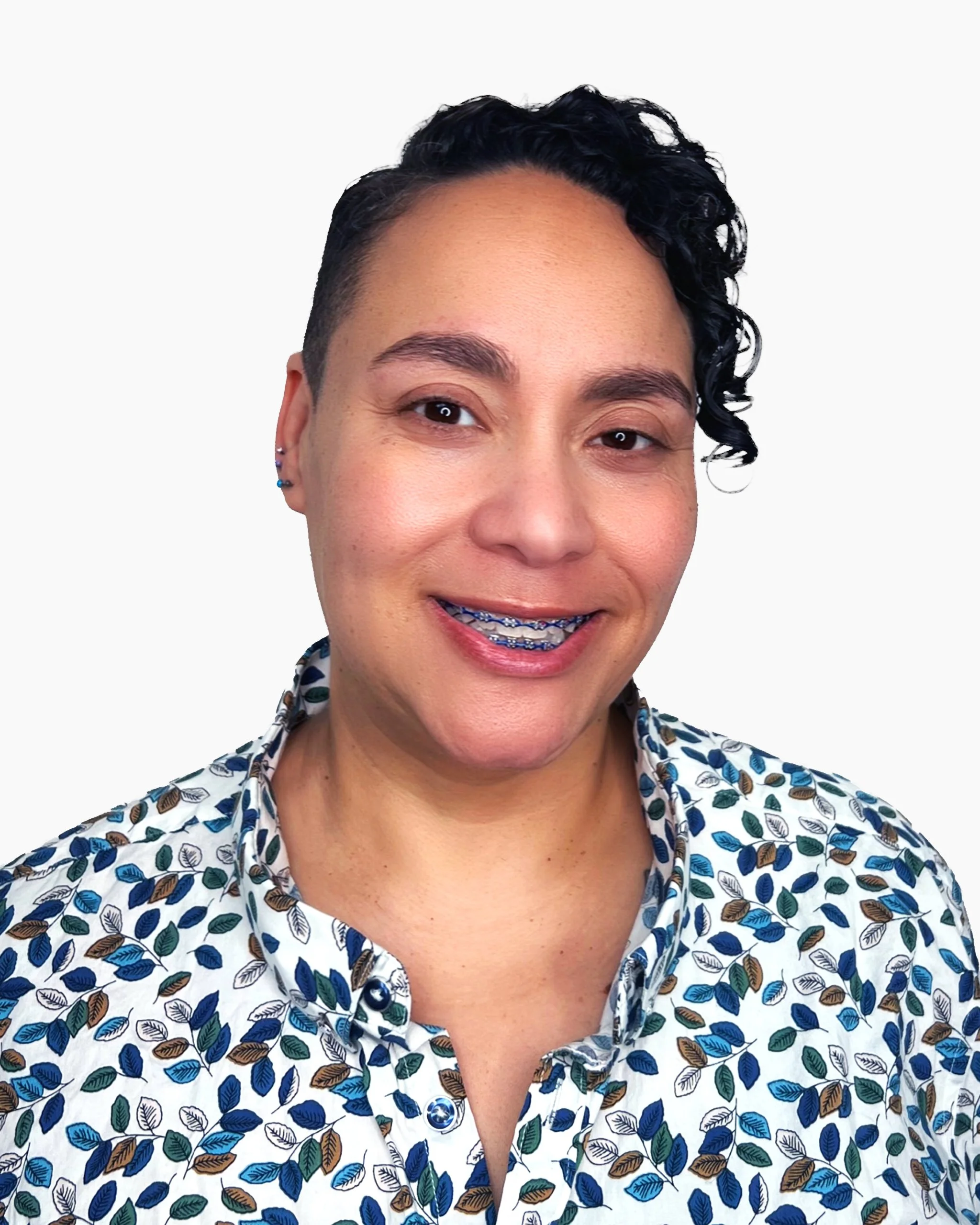 A woman with short dark curly hair, braces, and wearing a button-up shirt with a blue and white leaf pattern.