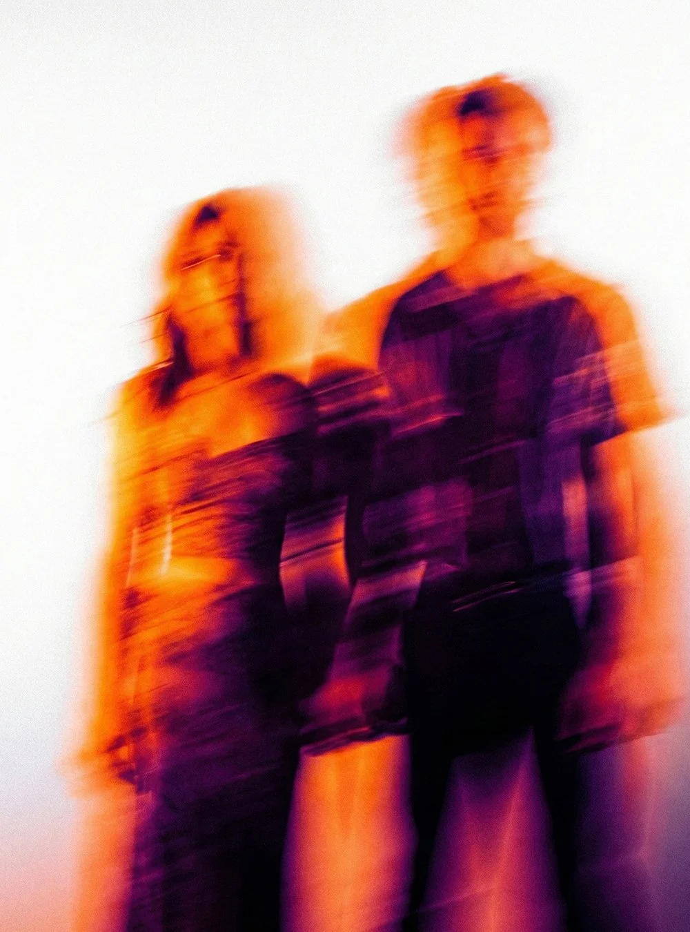 Dos personas de pie contra un fondo claro, con efecto de movimiento borroso y colores anaranjados y morados.