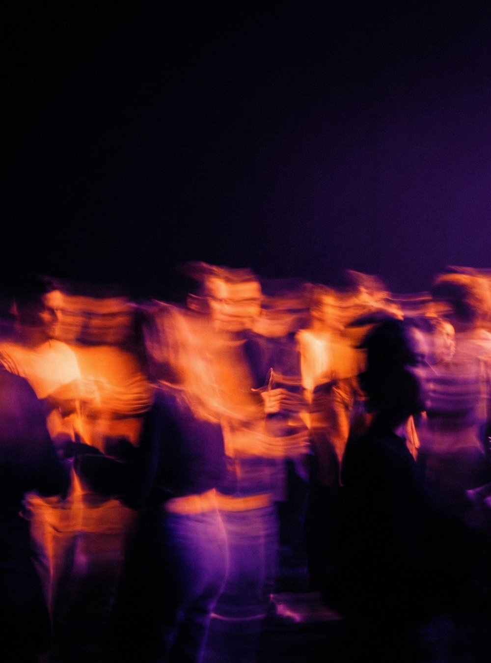 Grupo de personas en un evento nocturno con iluminación púrpura y azul, con movimiento y falta de enfoque.