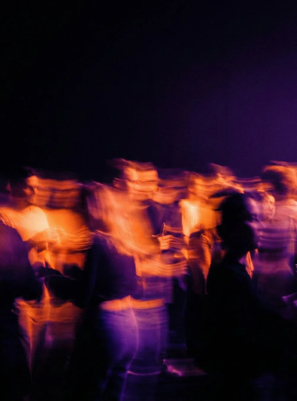 Grupo de personas en movimiento en un evento nocturno con iluminación de luces violetas y anaranjadas.