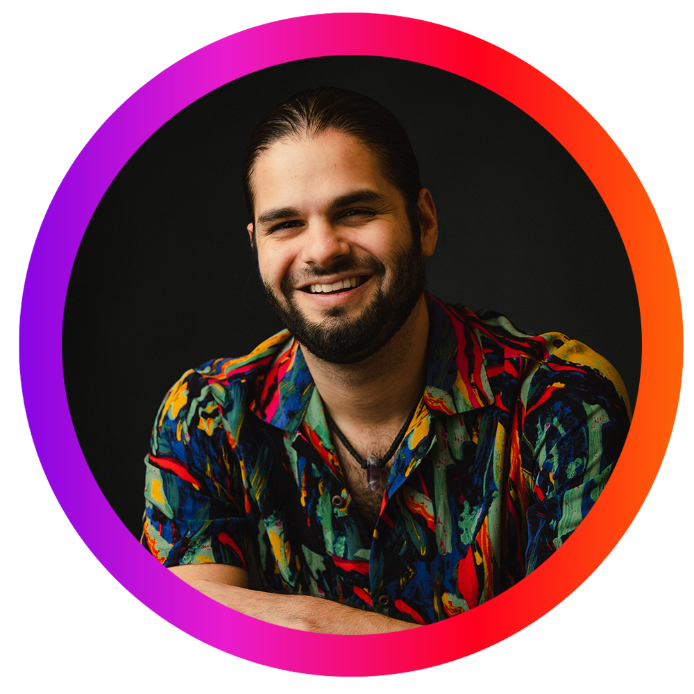 Retrato de un hombre joven con barba, sonriendo, llevando una camisa colorida con un fondo negro y un diseño de arcoíris enmarcando la imagen.