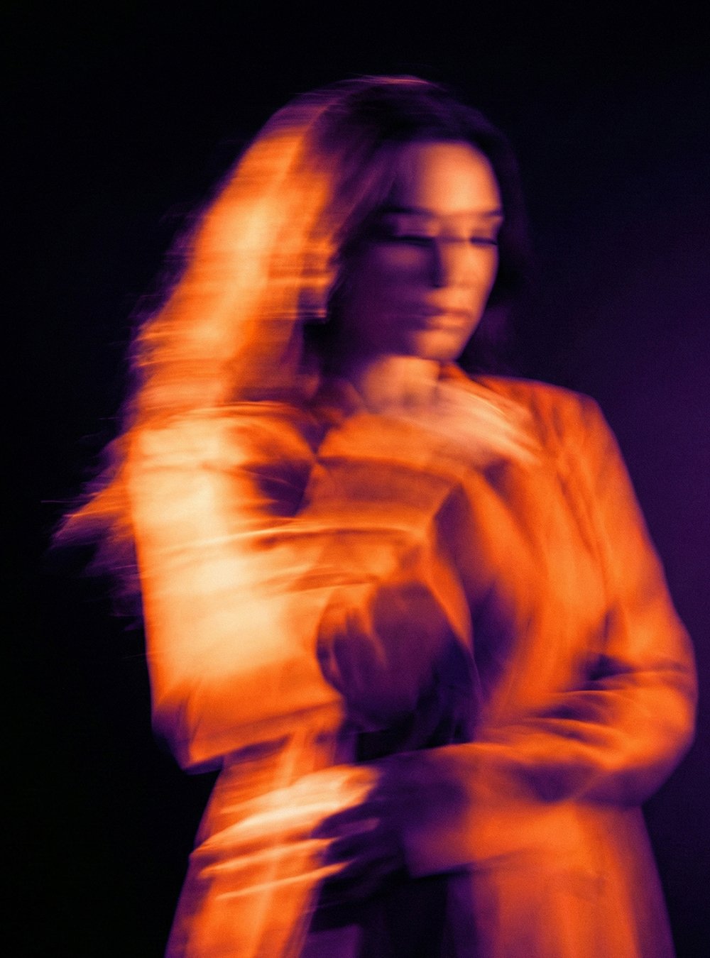 Mujer con movimiento en un fondo oscuro, con luz morada y naranja.