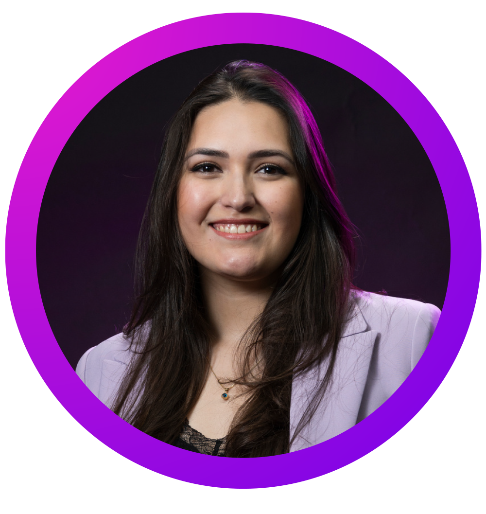 Retrato de una mujer joven con cabello largo y oscuro, sonriendo, vestida con una chaqueta gris clara y un top negro, fondo oscuro, y borde púrpura roto en la parte superior izquierda.