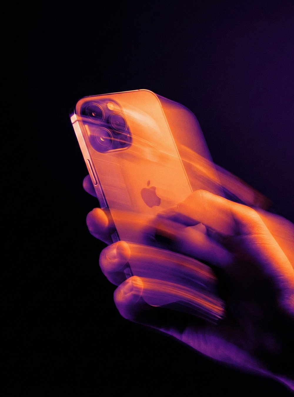 Una mano sosteniendo un iPhone 13 Pro en un fondo oscuro con efectos de movimiento en tonos morados y naranjas.