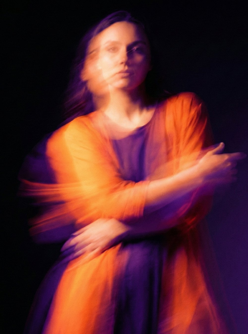 Retrato artístico de una mujer con movimiento y desenfoque, vestida con ropa naranja y fondo negro