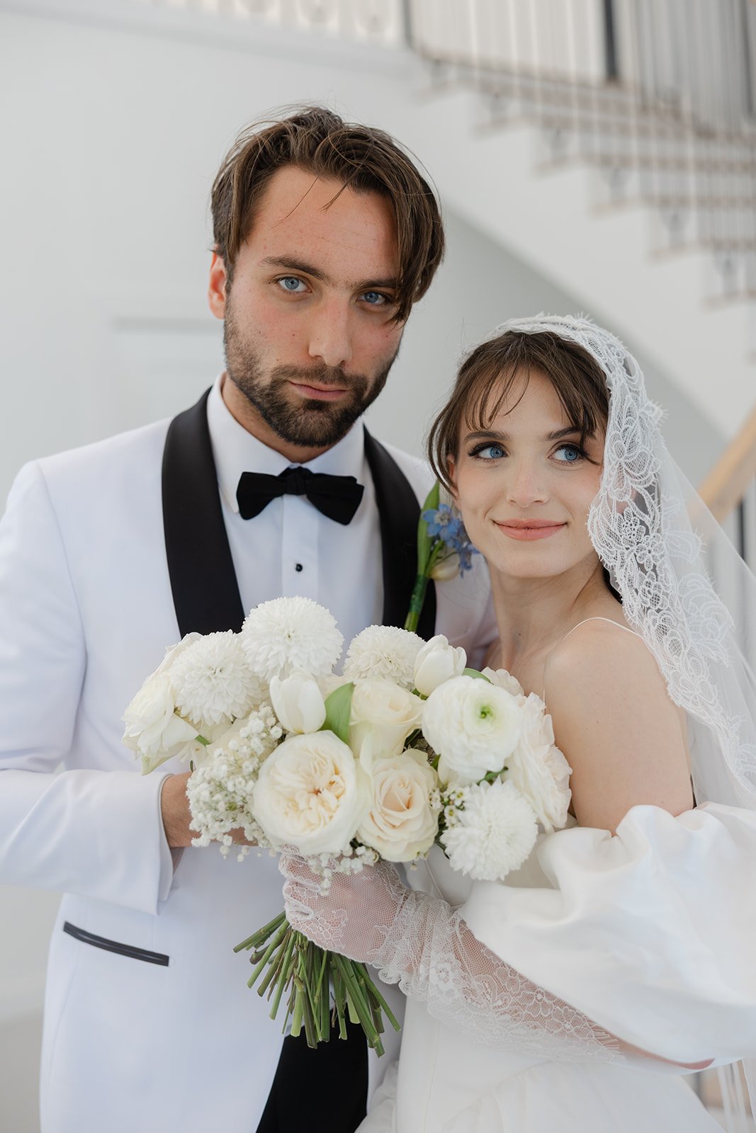 A bride and groom dressed in wedding attire holding a bouquet of white flowers.