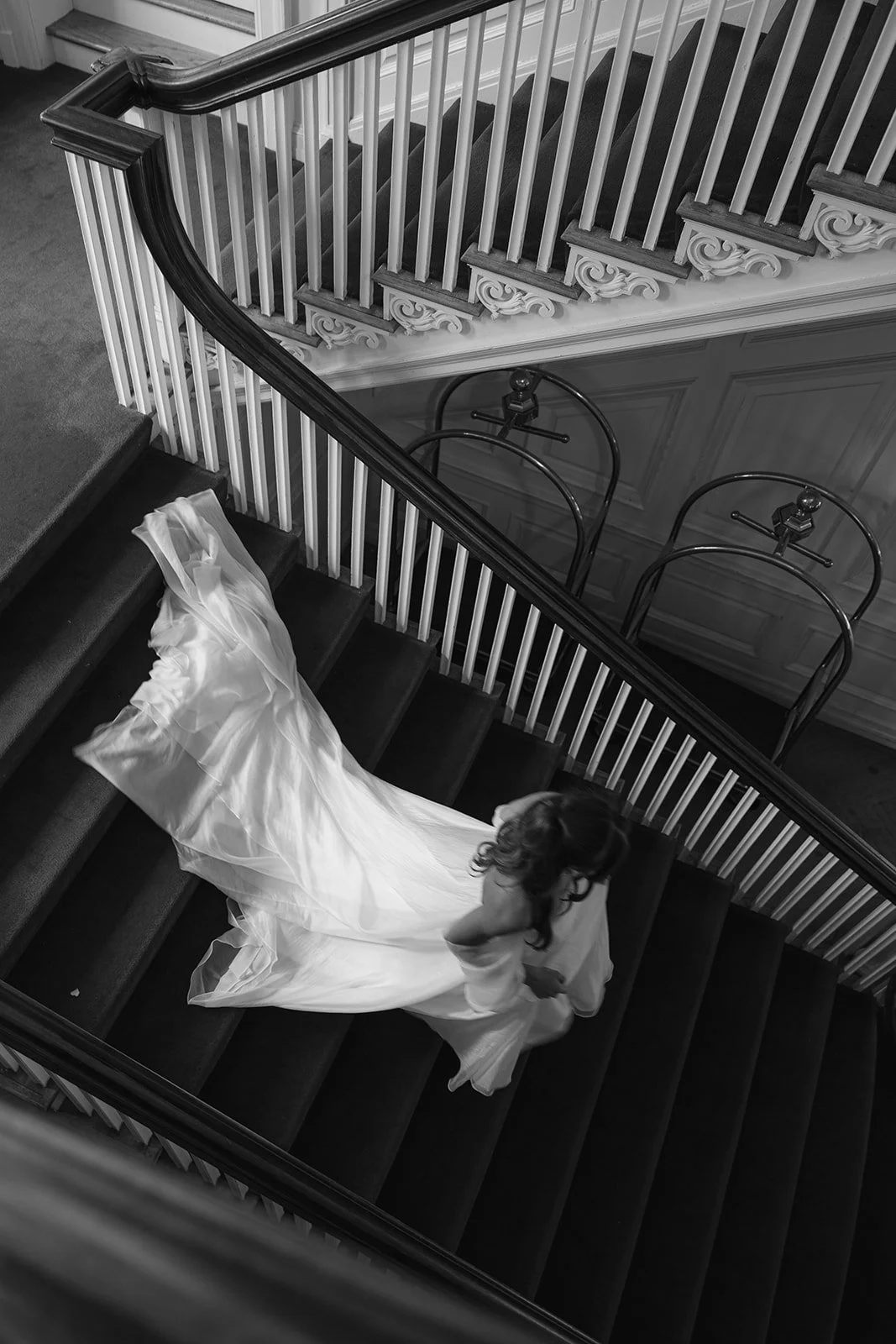 A woman in a flowing wedding dress walking up a staircase viewed from above.