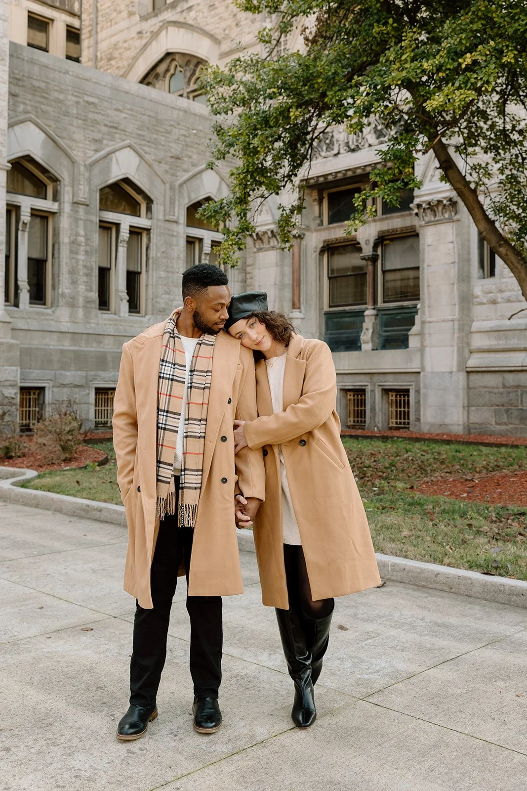 A happy couple in beige coats walking arm in arm outside a historic building, enjoying a cold day.