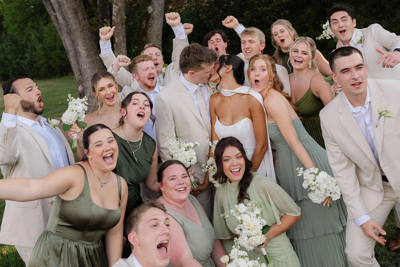 Group of wedding guests, including the bride and groom, celebrating outdoors with joyful expressions and raised fists.