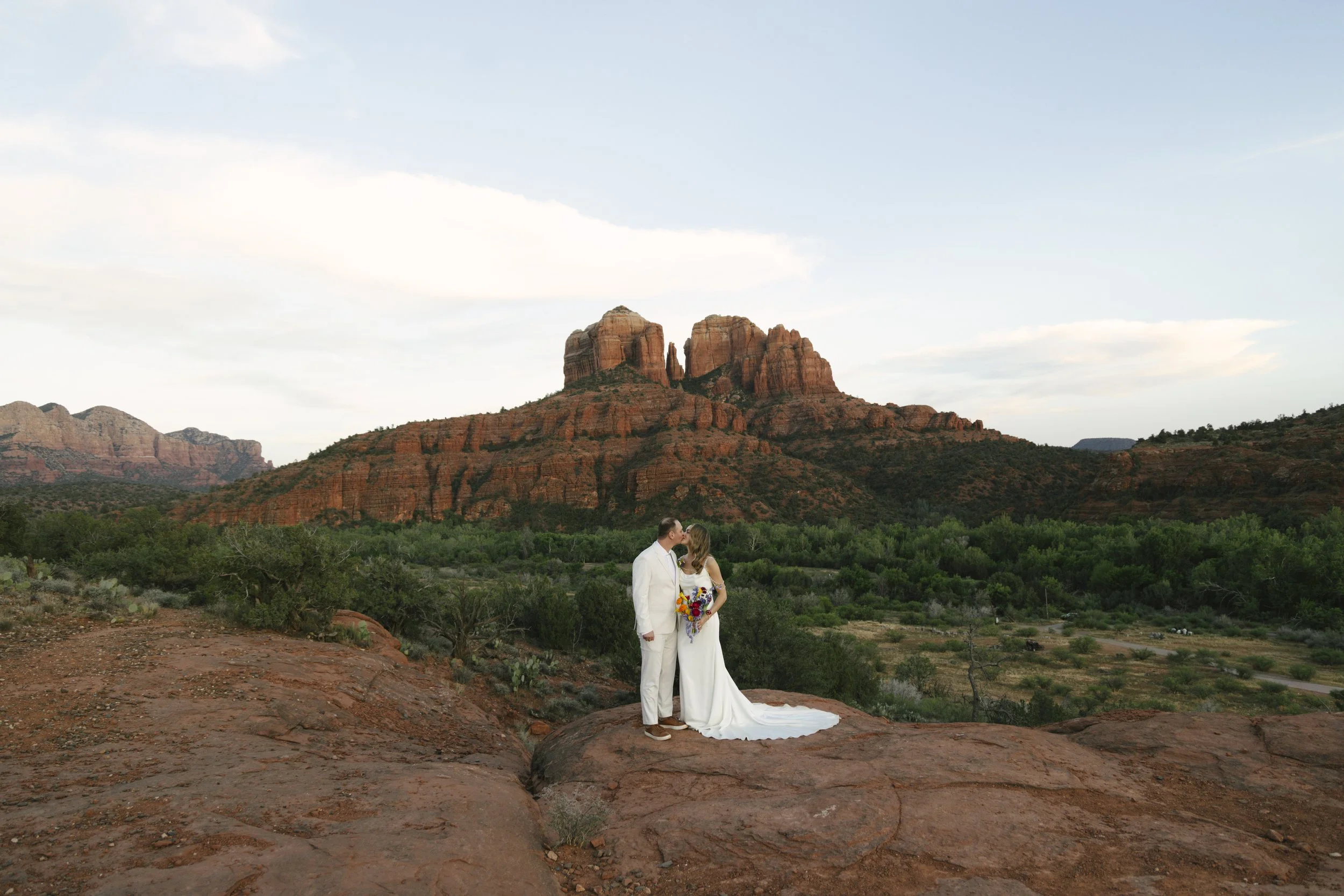 Bride and groom sharing a kiss during a Sedona, Arizona wedding with the iconic red rock mountains in the background, captured in a candid documentary style by Raw By Laura
