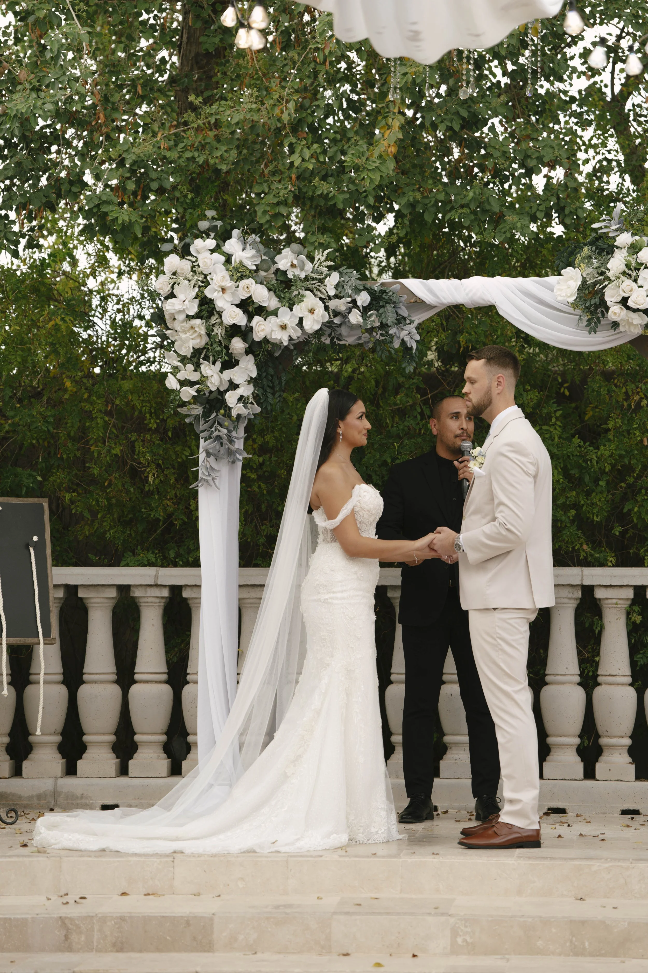 The bride and groom’s ceremony at Ashley Castle in Chandler, Arizona, was beautifully documented through hybrid film and digital photography, capturing their vows, ring exchange, and heartfelt moments beneath a romantic floral altar in the castle’s e