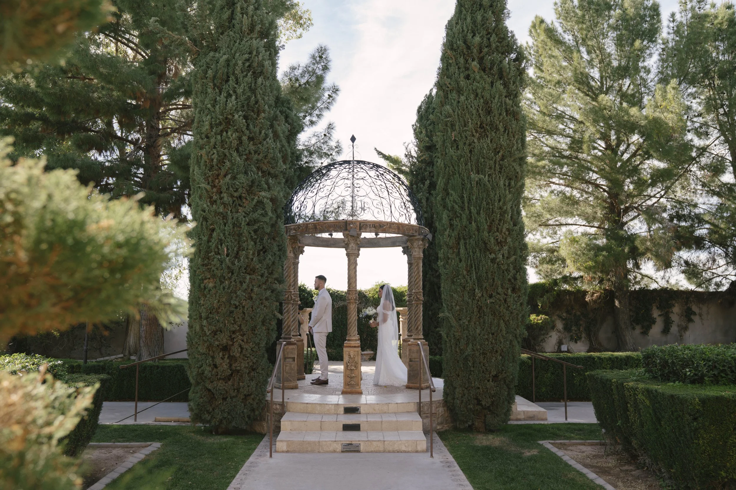 The bride and groom’s first look at Ashley Castle in Chandler, Arizona, unfolded in the venue’s romantic garden gazebo, where hybrid film and digital photography captured their emotional private reveal with timeless elegance, natural light, and intim