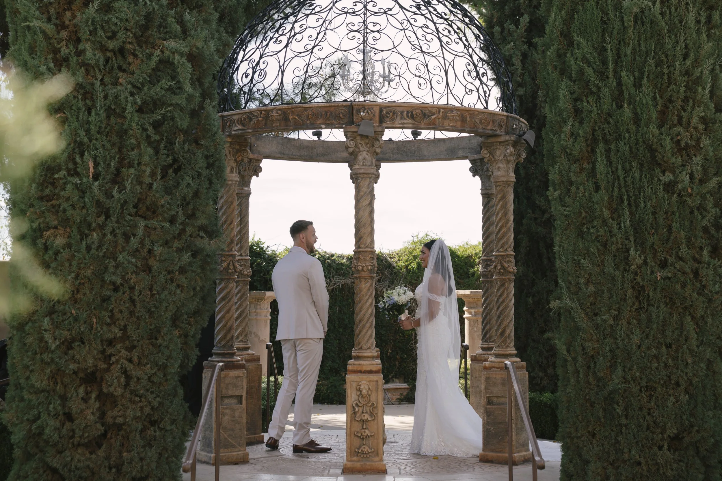 The bride and groom’s first look at Ashley Castle in Chandler, Arizona, unfolded in the venue’s romantic garden gazebo, where hybrid film and digital photography captured their emotional private reveal with timeless elegance, natural light, and intim