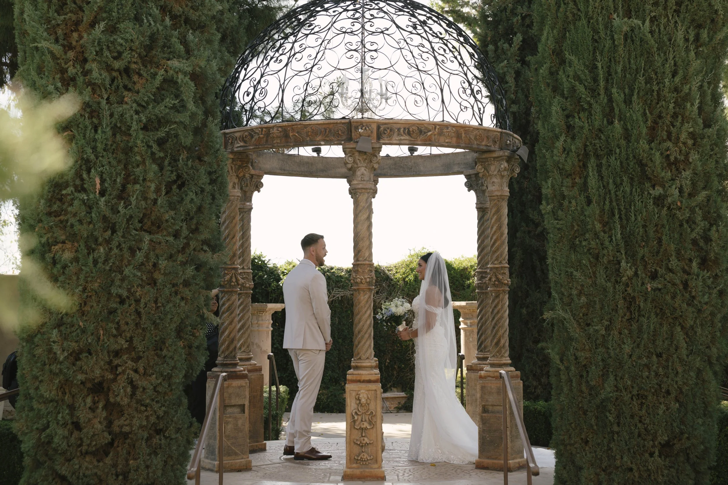 The bride and groom’s first look at Ashley Castle in Chandler, Arizona, unfolded in the venue’s romantic garden gazebo, where hybrid film and digital photography captured their emotional private reveal with timeless elegance, natural light, and intim