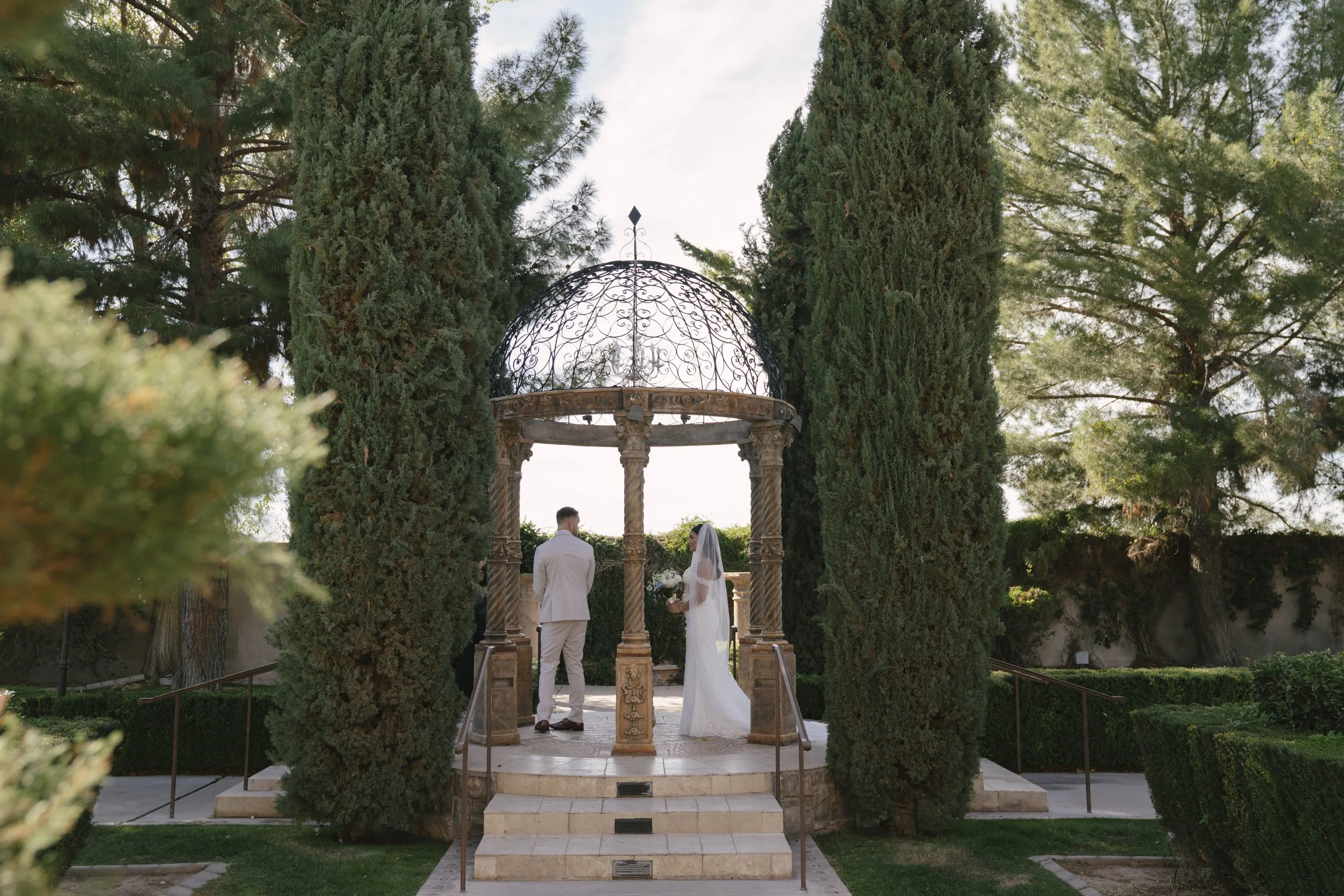 The bride and groom’s first look at Ashley Castle in Chandler, Arizona, unfolded in the venue’s romantic garden gazebo, where hybrid film and digital photography captured their emotional private reveal with timeless elegance, natural light, and intim
