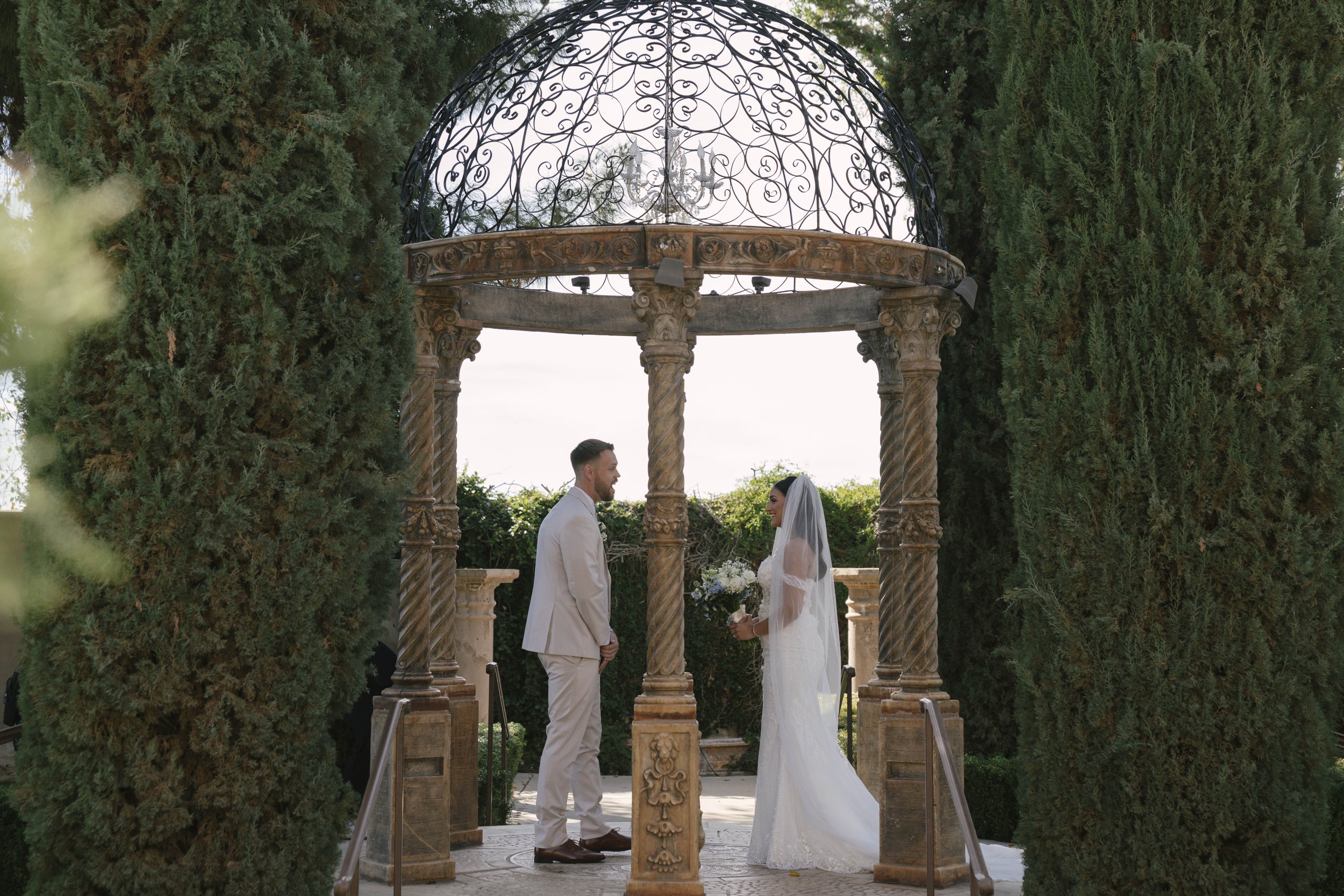 The bride and groom’s first look at Ashley Castle in Chandler, Arizona, unfolded in the venue’s romantic garden gazebo, where hybrid film and digital photography captured their emotional private reveal with timeless elegance, natural light, and intim