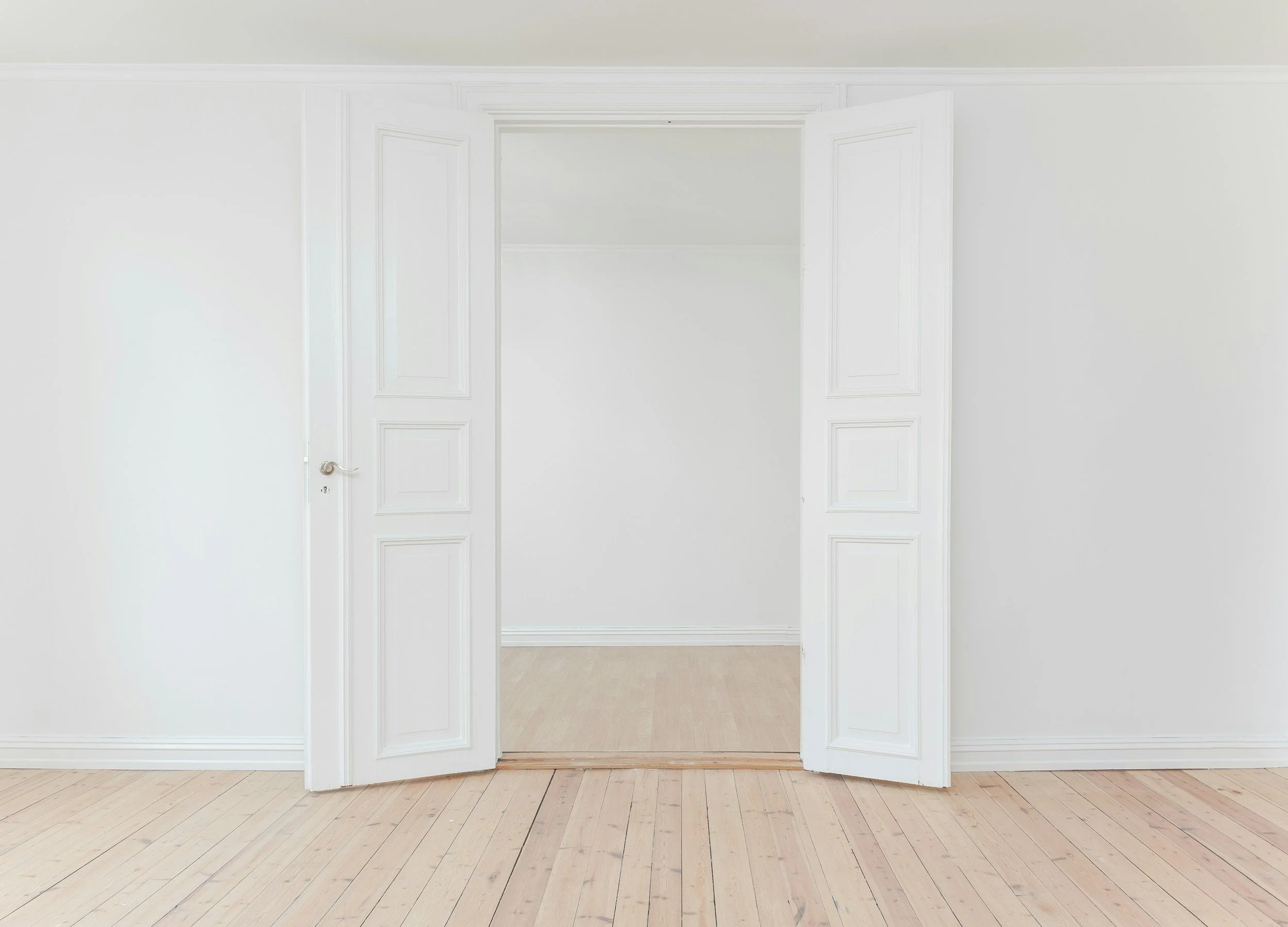 Open white double doors leading to another room with light-colored wood floors and white walls.
