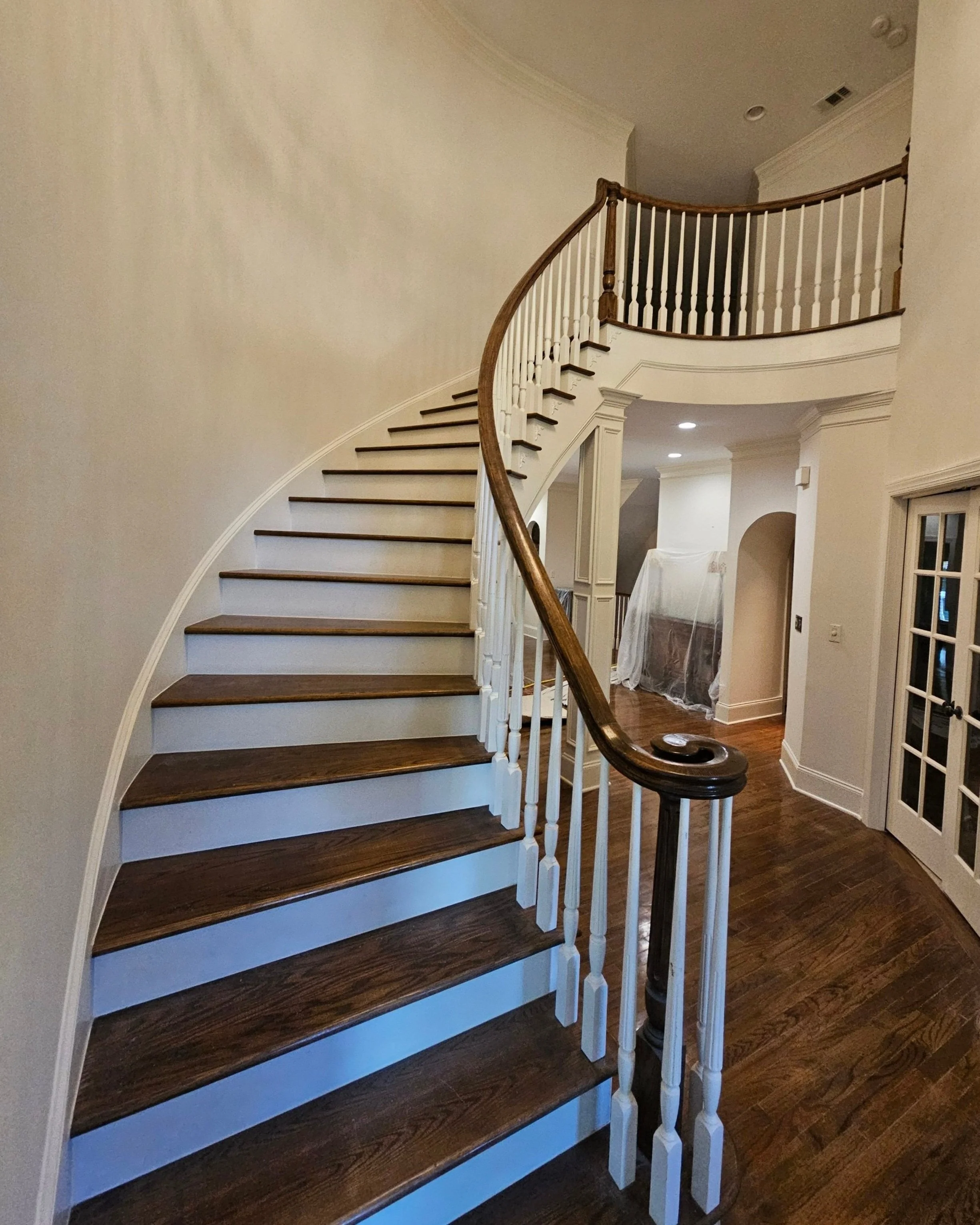 Interior view of a curved staircase with wooden steps, white risers, and a dark wooden handrail in a home.