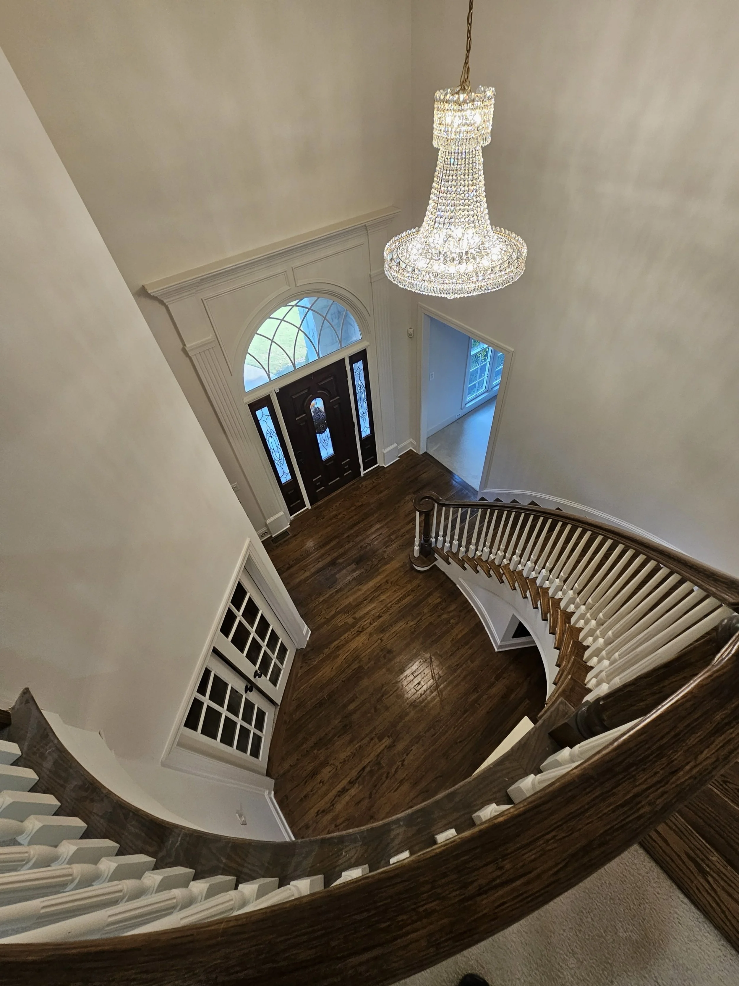 View of a grand foyer with a staircase, chandelier, front door with stained glass, and hardwood floors.