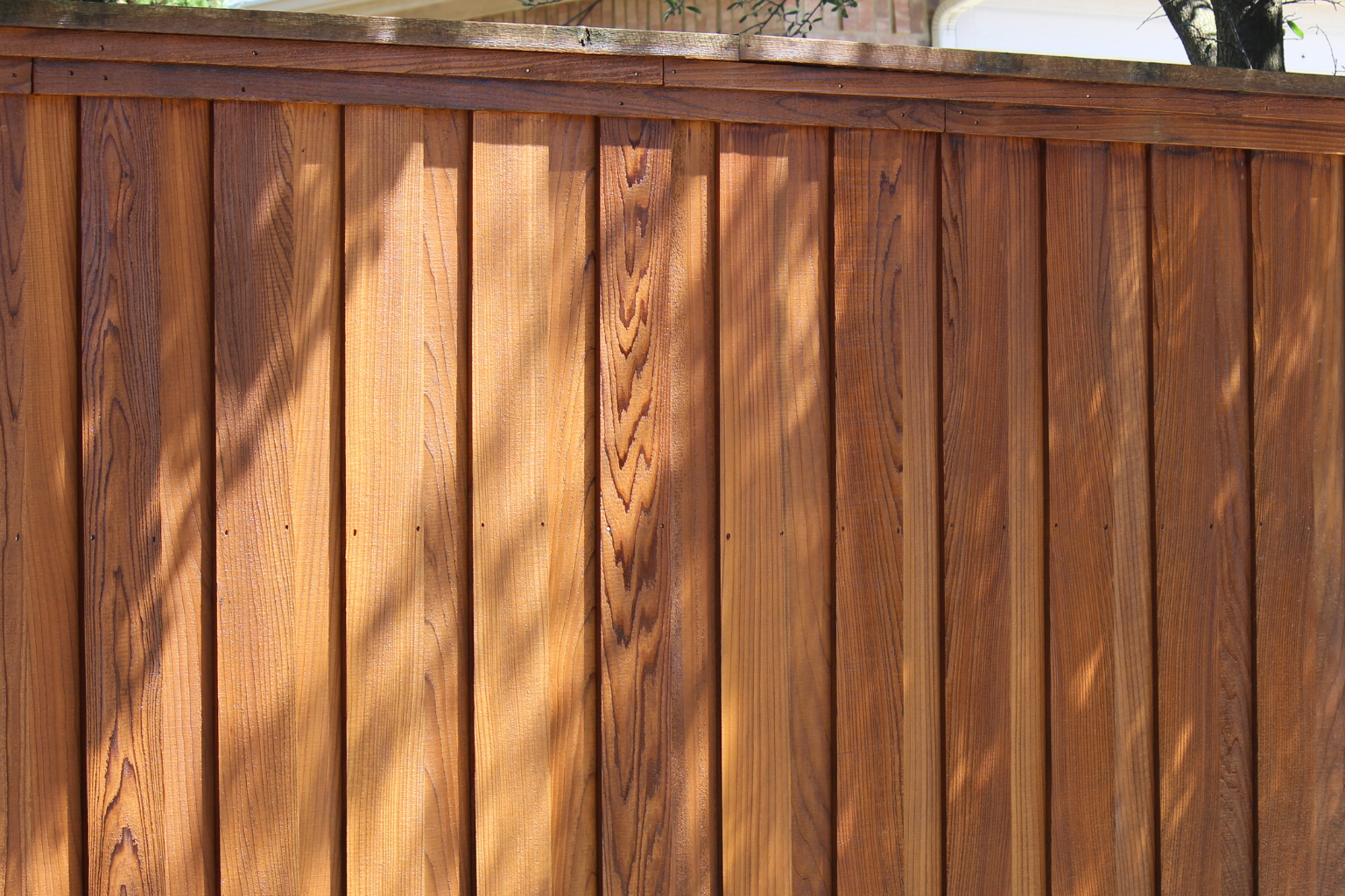 Close-up view of a wooden fence with vertical planks and a top rail, sunlight casting shadows on the wood.