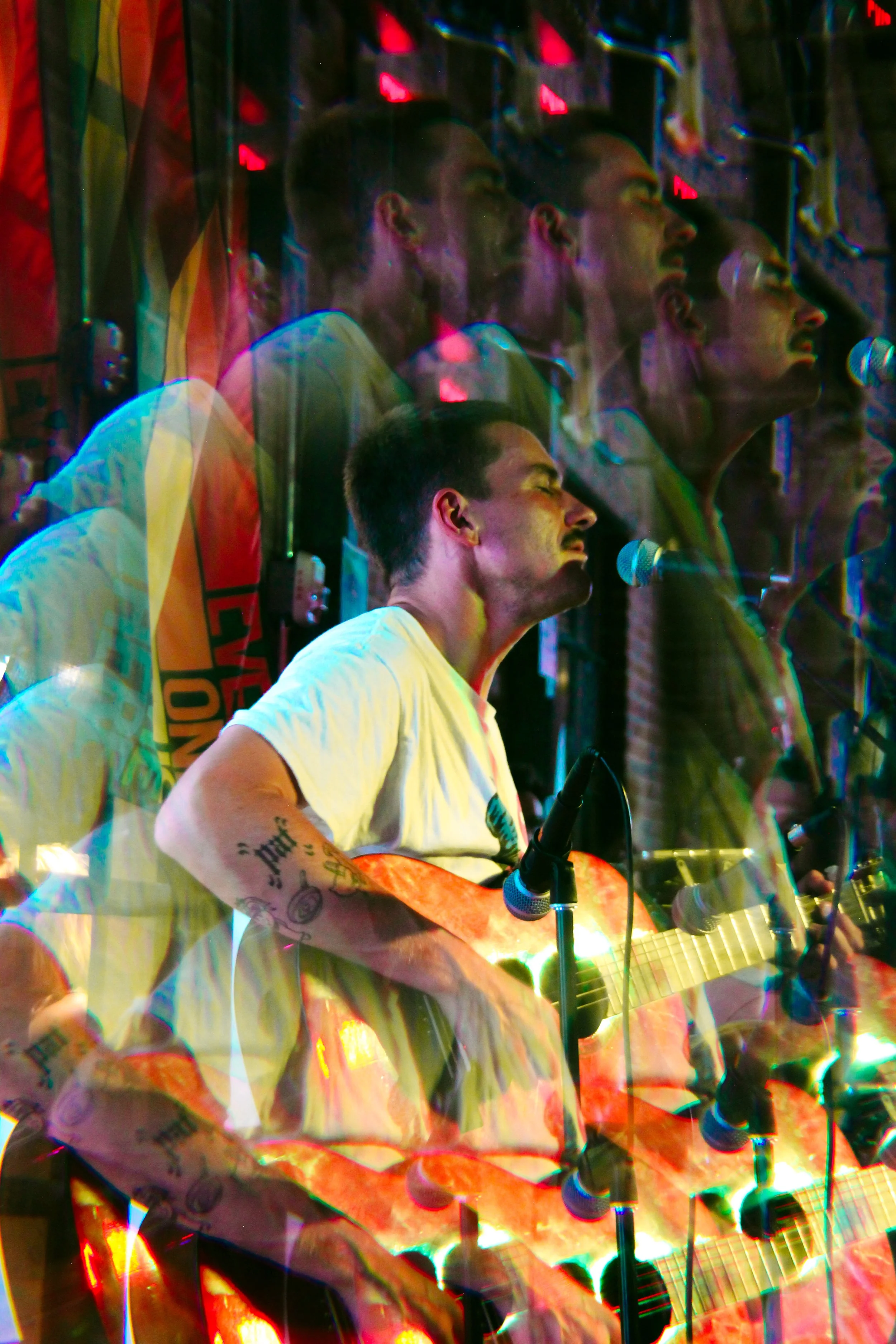 Medium Build performing live with an acoustic guitar under colorful stage lighting at Garage Sale Bar in East Nashville.