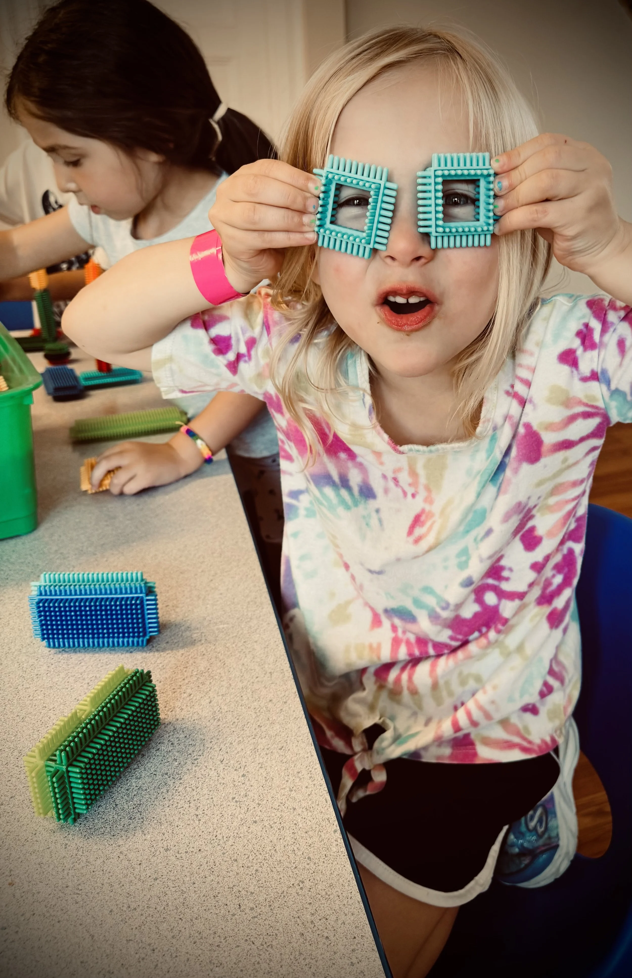 Two young girls playing with colorful magnetic building tiles at a table.