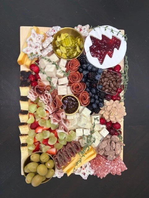 Charcuterie board with cheese, grapes, berries, meats, pickles, and various dips and crackers.