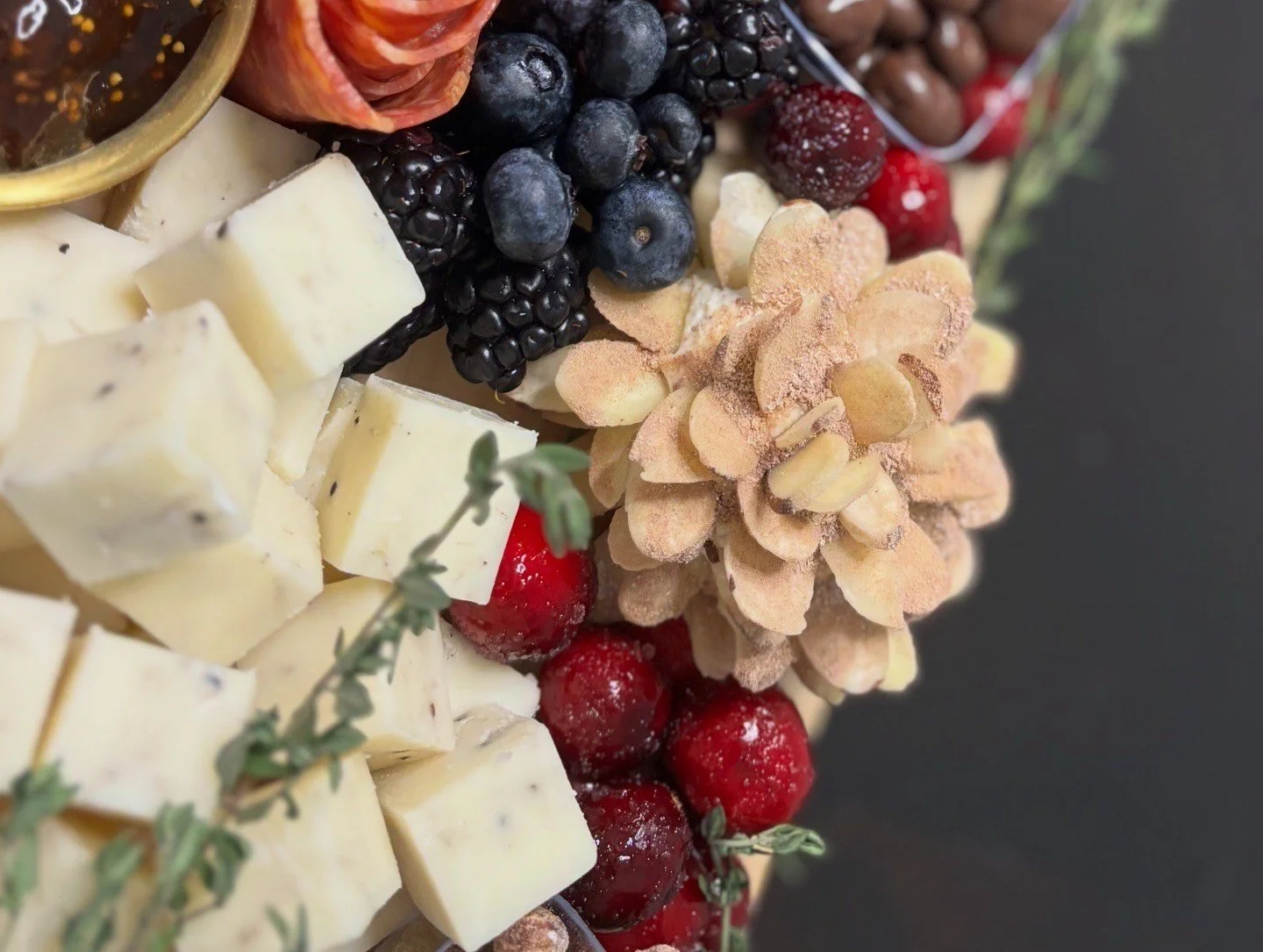 Close-up of assorted cheeses, fresh blackberries, blueberries, red berries, almonds, and a pine cone on a black background.