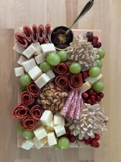 Charcuterie board with rolled salami, cubes of cheese, green grapes, nuts, and small red berries, topped with a spoonful of jam.