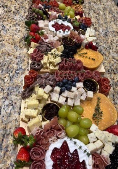 Charcuterie board with grapes, cheese, crackers, strawberries, and garnishes arranged in a line on a granite countertop.