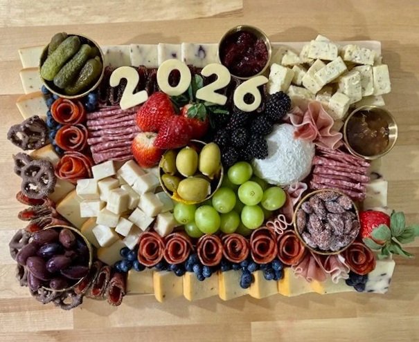 A cheese and charcuterie board with strawberries, grapes, blackberries, and various cheeses, decorated with the numbers '2026' in the center.