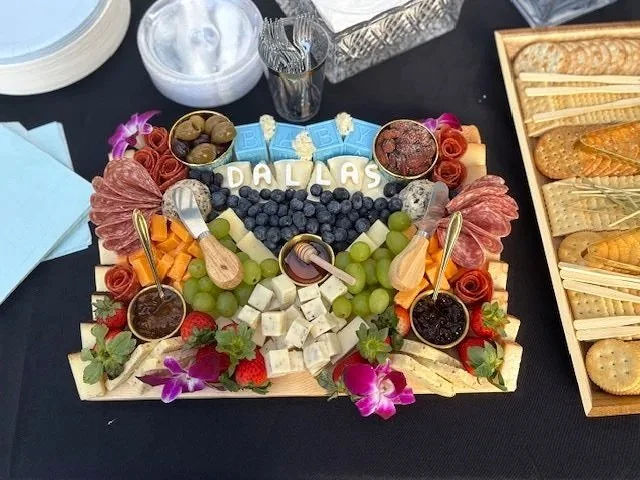 Charcuterie and cheese board with grapes, blueberries, strawberries, olives, assorted cheeses, sliced meats, crackers, and decorative flowers, with 