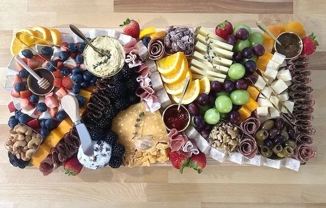 A cheese and fruit platter with various cheeses, fresh fruits like grapes, strawberries, blueberries, and blackberries, nuts, dips, and rolled deli meats.