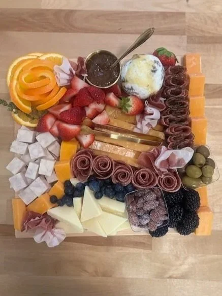 An assortment of cheeses, strawberries, blueberries, blackberries, grapes, sliced oranges, and rolled meats on a wooden surface, with a small bowl of honey and a scoop of ice cream.