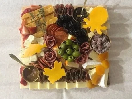 Assorted cheese, fruit, and charcuterie platter with blackberries, green grapes, sliced fruits, and decorative cheese shapes.