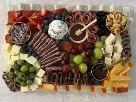 A charcuterie board with various cheeses, meats, fresh fruits, nuts, and honey.