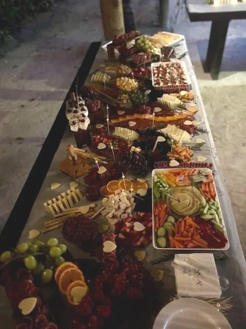 Charcuterie and cheese platter with fruit, vegetables, dips, and assorted snacks on a long table.
