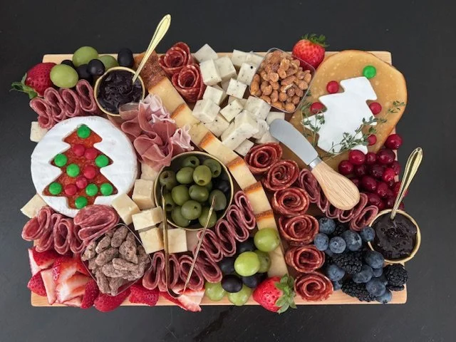 Charcuterie board with cheeses, meats, fruits, nuts, and garnishes.