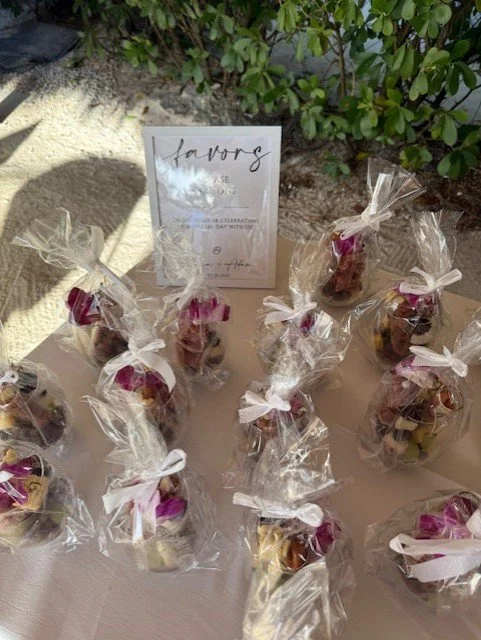 Small gift bags filled with assorted chocolates, tied with white ribbons, placed on a table with a sign that reads 'Favor' for a celebration event.