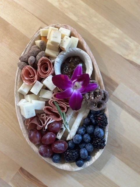 An assorted cheese and fruit platter with grapes, blueberries, blackberries, and a purple orchid flower
