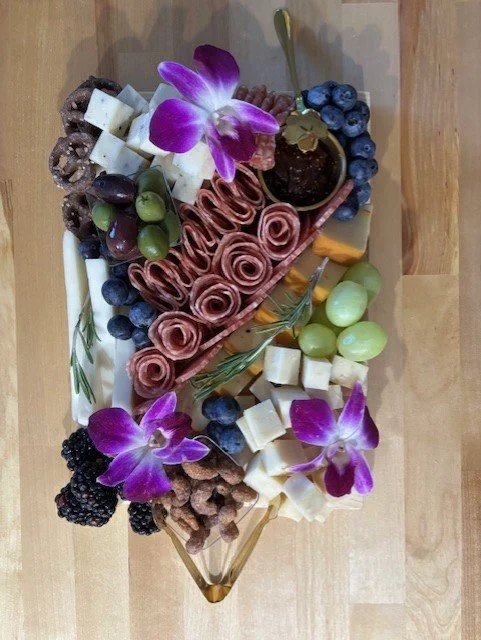 Assorted cheese, grapes, blackberries, blueberries, olives, and edible flowers on a serving platter.